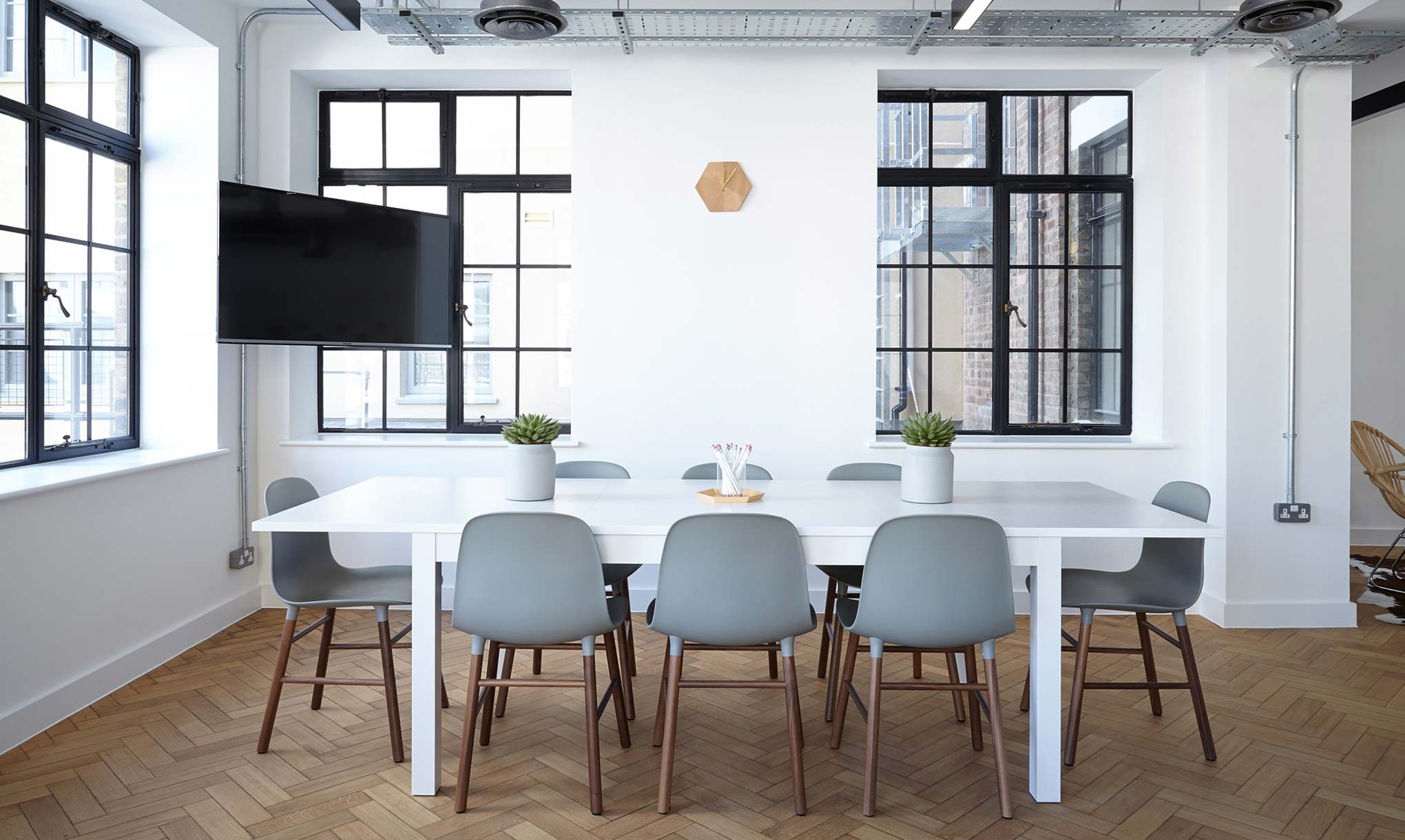 Salle à manger style industriel, grand écran plat fixé en hauteur, pièce lumineuse, parquet en bois, huit chaises en bois design